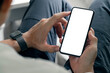 © NAMPIX - Cropped shot of man hands using smartphone with blank screen while sitting in living room at home.