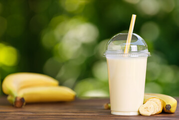 Wall Mural - banana milkshake in disposable plastic glass on wooden table