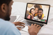 © Prostock-studio - African American man having video call with multiracial young family, lying on bed with laptop