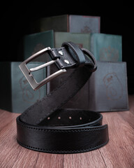 A black leather belt with a steel buckle rests on a wooden table