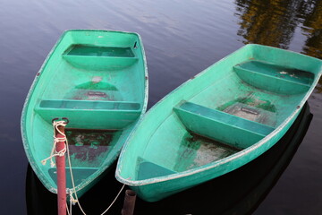 Two empty green rowing boats without oars on the calm water in the parked near the shore at summer day