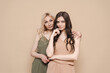 © diignat - Blonde mother and brunette adult daughter wearing identical clothes, different colors, posing over beige background