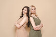 © diignat - Blonde mother and brunette adult daughter wearing identical clothes, different colors, posing over beige background