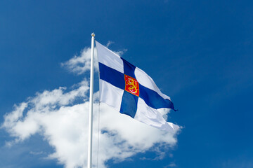 Wall Mural - State flag of Finland with national coat of arms against blue sky on the wind