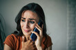 © My Ocean studio - Sad, frustrated young brunette woman is crying with smartphone in hands while she sitting on the chair at apartment