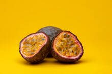Cut In Half Maracuja Or Brazilian Tropical Passion Fruit Studio Food Still Life Against A Yellow Background Showing Pulp Flesh And Black Seeds Inside With An Intact Specimen Behind