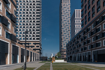 A capture of a courtyard in a modern residential area with a pedestrian zone and a geometric pattern of paving slabs with green lawns surrounded by tall houses