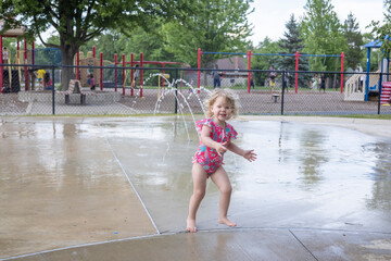 Wall Mural - 2 year old girl playing at the splash pad at a water park in her bathing suit