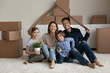 © fizkes - Portrait of smiling young Caucasian family with two teen children sit on floor hold paper roof moving relocating to new home. Happy parents with teenage kids in own house. Rent, realty concept.