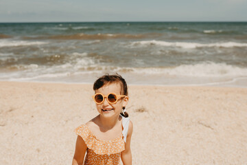 Portrait six year girl in yellow swimsuit wearinmg sunglasses on the beach. hot summer day.