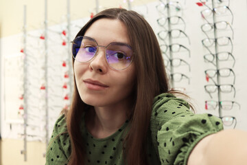 Canvas Print - A young woman takes a selfie photo while trying on and choosing new glasses at an optical retail store