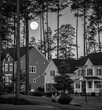 Black and white image of full moon rising over residential houses