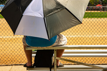  Person sitting enjoying ballgame using umbrella on warm summer day.