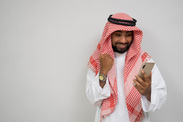 an arabian young man in a turban using a mobile phone happily looking at the screen with an excited expression on a plain background