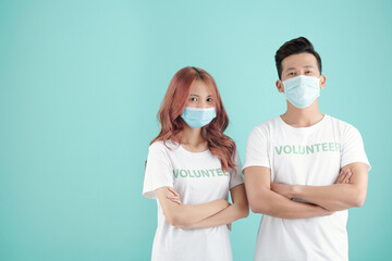 Poster - Young couple standing in protective masks and volunteers t-shirts, crossing arms and looking at camera