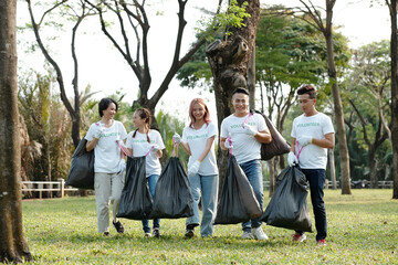 Wall Mural - Smiling college students volunteering in city park or on campus and collecting garbage in big trash bags