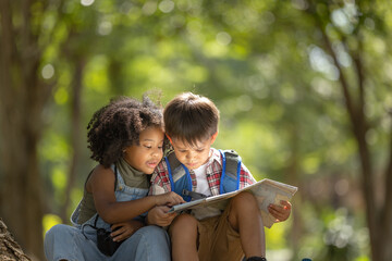 multi-ethnic children in casual clothing sitting on tree roots, looking at the map with interest.exp