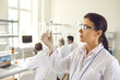 © Studio Romantic - Side view young female scientist in coat, gloves and goggles looking at small green leaf inside test glass tube in her hand. Nature and science, using plants in cosmetology laboratory research concept
