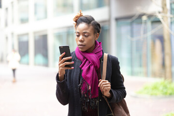 Wall Mural - Black woman walking on city street holding mobile phone in hand