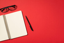 Top View Photo Of Black Glasses Pen And Open Spiral Notebook On Isolated Vivid Red Background With Blank Space