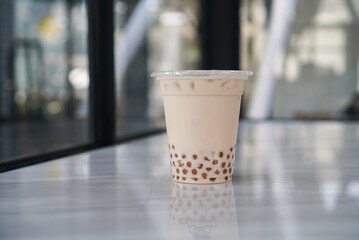 Wall Mural - Iced Milk Tea with golden bubble. A plastic cup of milk tea with bubble/boba (golden pearl) on table.