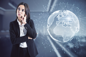 Poster - Thoughful young european businesswoman standing in blurry office interior with glowing globe hologram. Global business and innovation concept. Double exposure.