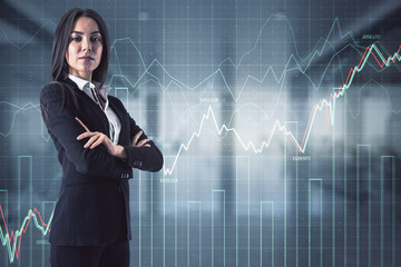 Attractive young european businesswoman with folded arms standing in blurry office interior with glowing forex chart hologram. Market and trade concept. Double exposure.