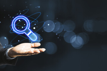 Poster - Businessman hand holding glowing magnifier icon hologram on blurry bokeh background with mockup place. Web browser and search engine concept.