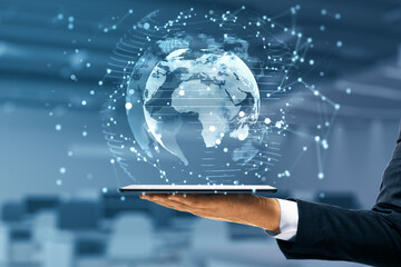 Poster - Businessman hand holding tablet with glowing globe interface on blurry office background. Global futuristic innovation concept. Double exposure.