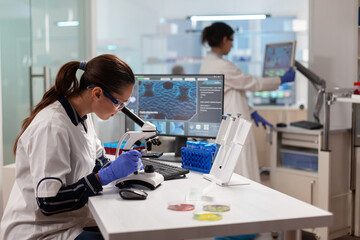 Wall Mural - Biotechnology scientist looking through microscope analyzing genetical material. Medicine, biotechnology researcher in advanced pharma lab, examining virus evolution.