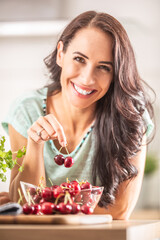 Wall Mural - Smiling woman picks two cherries from a seethrough bowl indoors