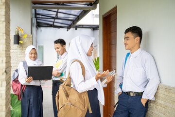 two pairs of teenagers in school uniforms with school bags chatting outside the classroom