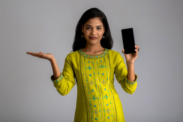 Young beautiful girl holding and showing blank screen of smartphone or mobile or tablet phone on a gray background.