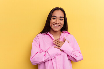 Wall Mural - Young mixed race woman isolated on yellow background has friendly expression, pressing palm to chest. Love concept.