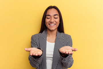 Wall Mural - Young mixed race woman isolated on yellow background holding something with palms, offering to camera.