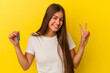 © Asier - Young caucasian woman holding a home keys isolated on yellow background joyful and carefree showing a peace symbol with fingers.