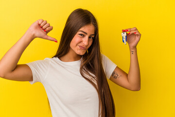 Wall Mural - Young caucasian woman holding a home keys isolated on yellow background feels proud and self confident, example to follow.