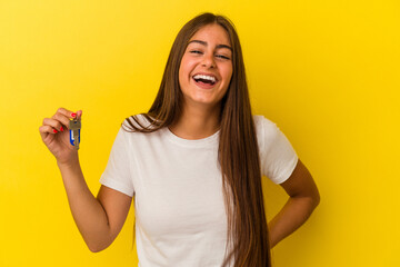 Wall Mural - Young caucasian woman holding a home keys isolated on yellow background laughing and having fun.