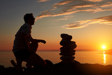 Wall Mural - Silhouette of a man and zen stones on a ocean sea cliff in sunset sunrise time.