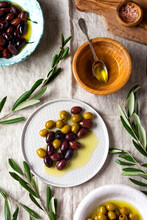 Several Varieties Of Fresh Olives In Different Ceramic Plates On An Old Vintage Gray Napkin Tablecloth Table Background. Natural Product Concept. Rustic Vintage Set Of Cutlery. Top View, Copy Space