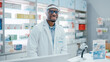 © Gorodenkoff - Pharmacy: Professional Confident Black Pharmacist Wearing Lab Coat and Face Shield, Looks at Camera Smiling Charmingly. Druggist in Drugstore Store with Shelves Medicine. Coronavirus Safety Measures