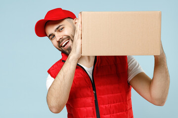 Wall Mural - Professional delivery guy employee man in red cap white T-shirt vest uniform workwear work as dealer courier hold blank cardboard box isolated on pastel blue color background studio. Service concept.