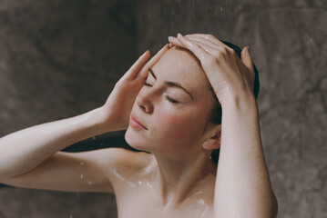 Close up half naked topless young relaxed woman 20s taking hot shower hold head close eyes water doing morning routine in bathroom brown background. Skin care healthcare cosmetic procedures concept