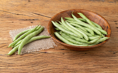 A group of green bean pods in a bowl over wooden table