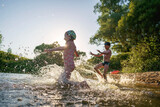 Fototapeta Łazienka - Happy children run from the shore into the water. Summer children's vacation on shore of a lake or river. boy and girl jump into water, swim and splash around at sunset. Active holidays. Dynamic image