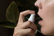 Woman taking homeopathic oral spray; background has ficus house plants