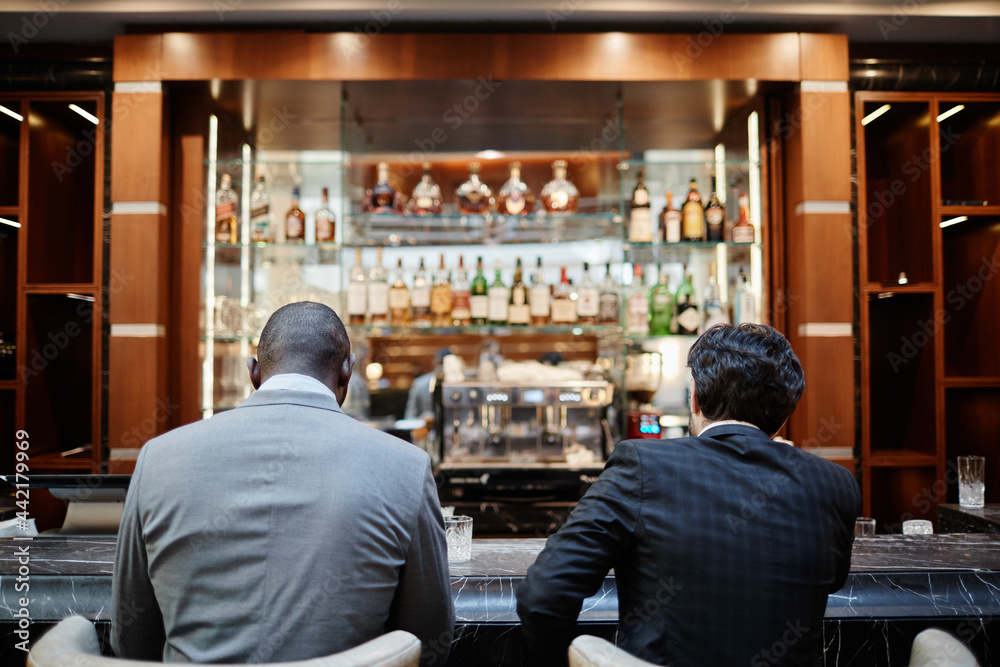 Back view portrait of two successful business people at bar in hotel lobby during business trip - obrazy, fototapety, plakaty 