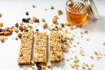 Normal view of granola or cereal bars with dried fruits and raisins with a jar of natural honey on a white surface. Natural eating concept.