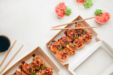 baked sushi set in paper packaging on white background - flat lay set with ginger and wasabi - bright delicious set of sushi rolls in a box