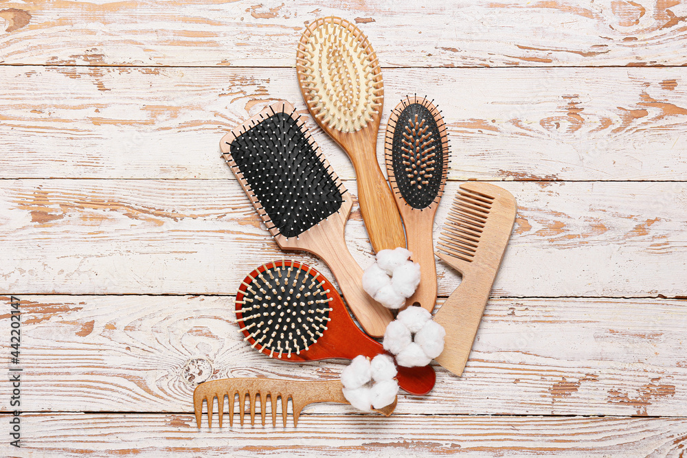 Composition with hair brushes, combs and cotton flowers on light wooden background